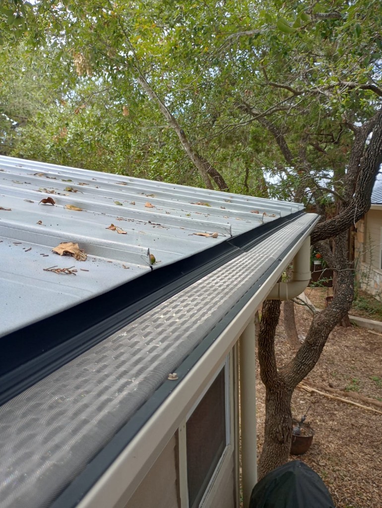 Hand removing dry autumn leaves from a roof-edge gutter during fall cleanup in Littleton